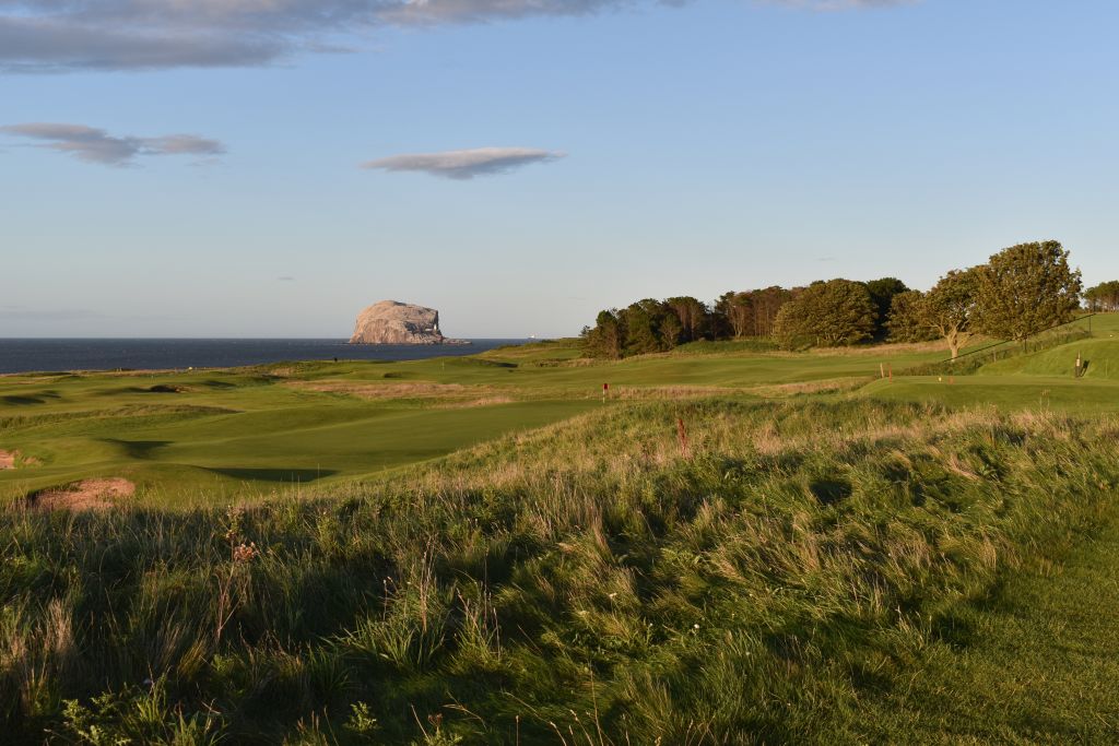 A breathtaking view of The Glen, with its rolling green hills and serene landscape, leading out to the iconic Bass Rock in the distance. The Bass Rock, a striking volcanic island, stands majestically in the Firth of Forth, creating a stunning contrast against the tranquil waters and the lush greenery of The Glen.