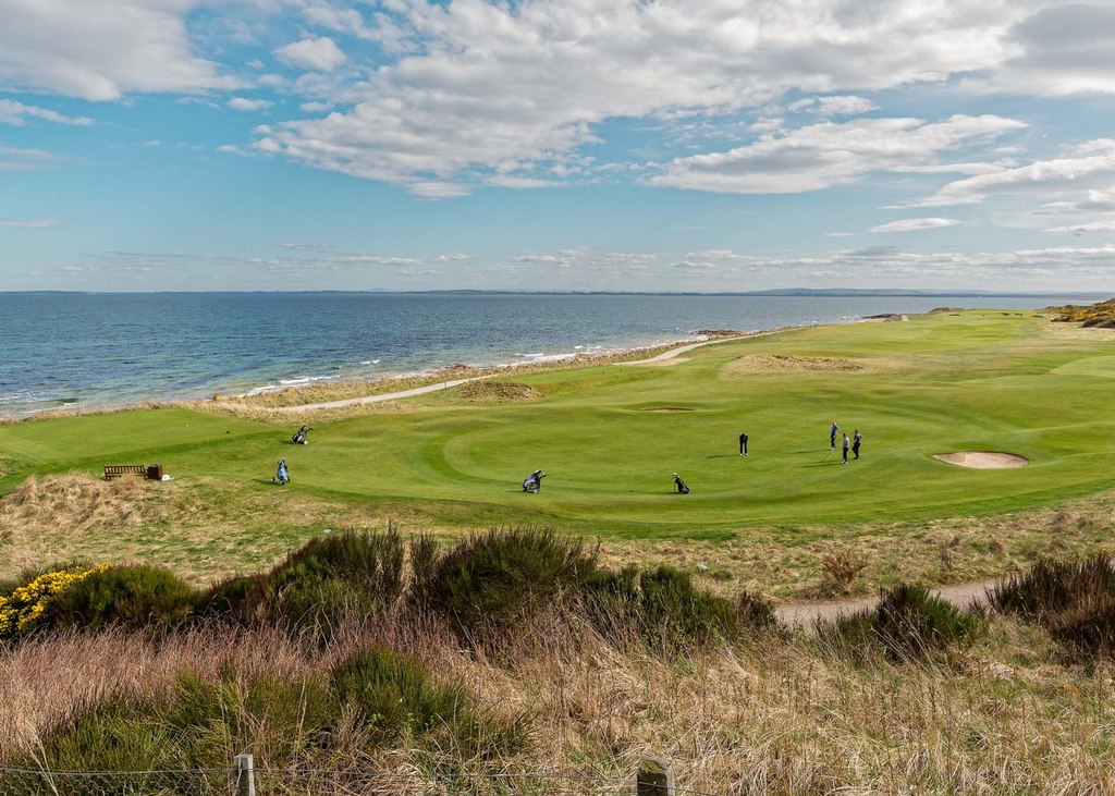 A scenic view of golfers playing the Royal Dornach golf course, with the sea in the background.