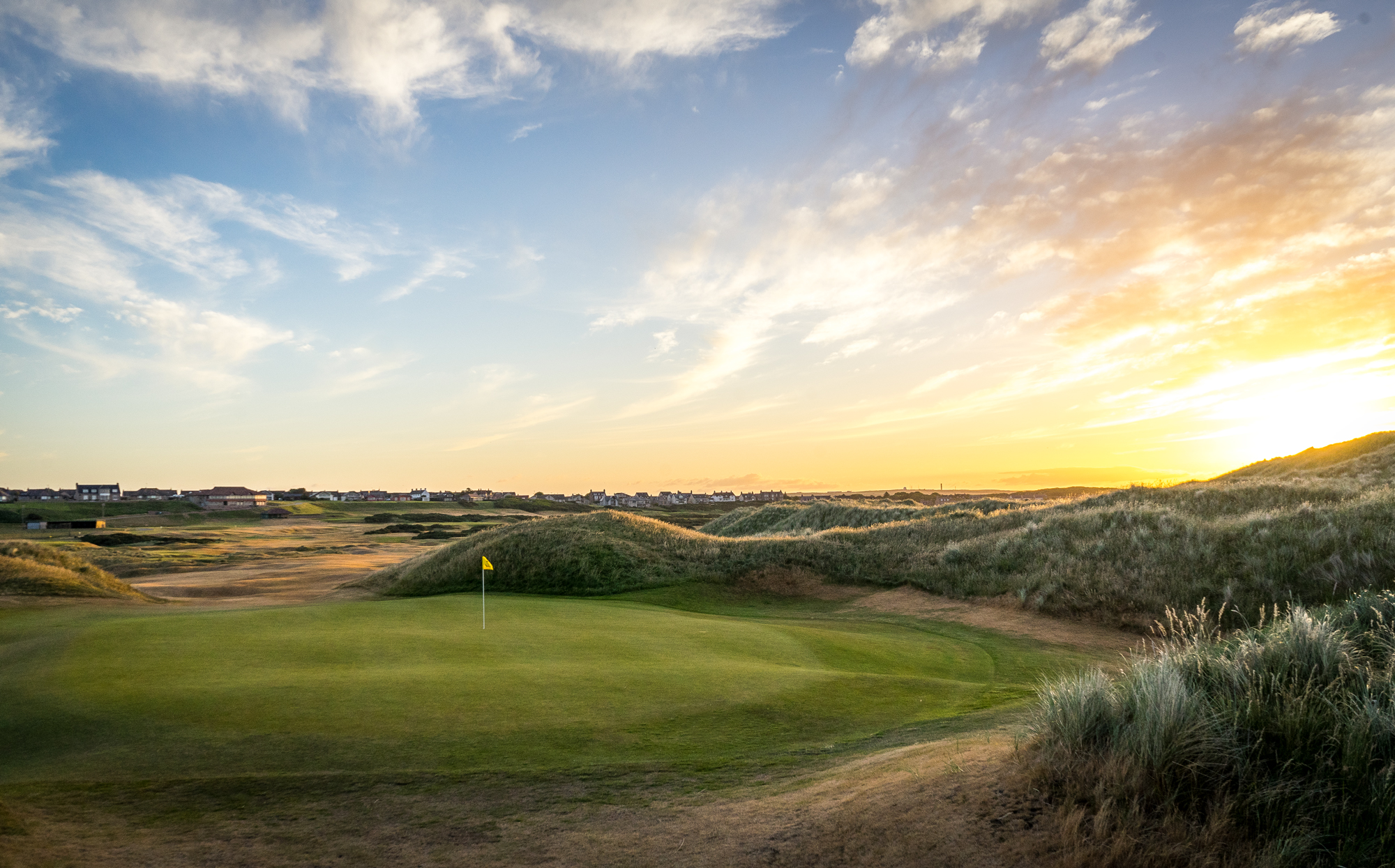 A breathtaking view of the 7th hole at Cruden Bay Golf course with the sun setting.