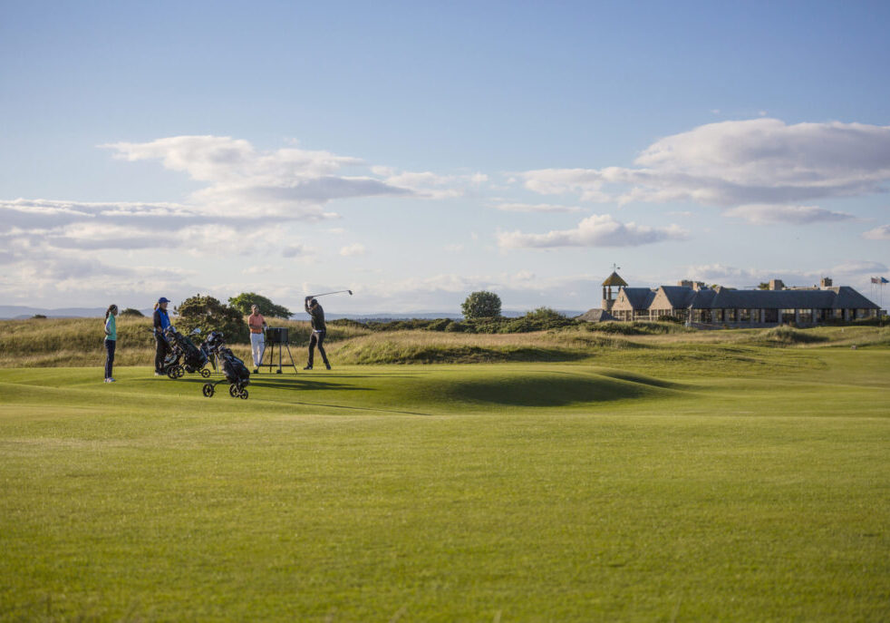 St. Andrews Old Course: The historic and iconic golf course with its rolling fairways, famous Swilcan Bridge, and the clubhouse in the distance, set against a backdrop of a clear blue sky.